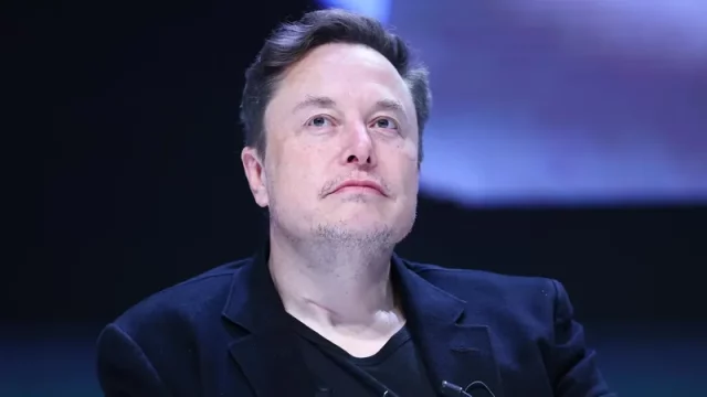 Elon Musk mengenakan jas hitam menatap ke atas dalam sebuah acara