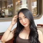 Sandrina Mazayya duduk di kursi berlengan sebuah kafe dengan jendela kaca besar di belakangnya.