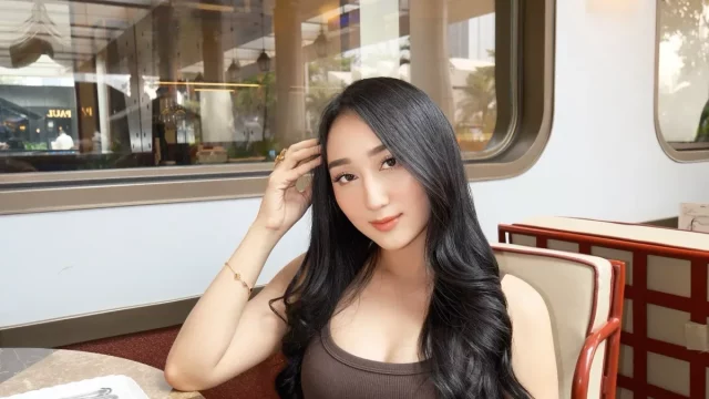 Sandrina Mazayya duduk di kursi berlengan sebuah kafe dengan jendela kaca besar di belakangnya.
