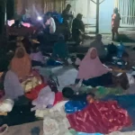 Warga terdampak gempa duduk beralaskan tikar dan terpal di luar rumah pada malam hari