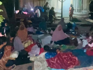 Warga terdampak gempa duduk beralaskan tikar dan terpal di luar rumah pada malam hari