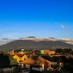 Gunung Marapi terlihat dari Bukittinggi dengan atap rumah warga di latar depan dan awan menggantung di lerengnya