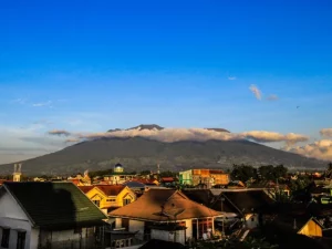 Gunung Marapi terlihat dari Bukittinggi dengan atap rumah warga di latar depan dan awan menggantung di lerengnya