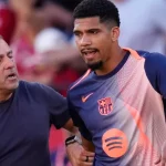 Seorang pelatih berbicara sambil merangkul seorang pemain bek yang mengenakan seragam latihan Barcelona