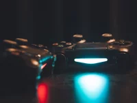 Dua stik pengendali konsol permainan dengan lampu biru menyala di atas permukaan gelap