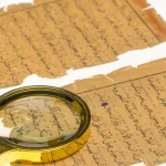 Dua lembar naskah kuno berbahasa Arab yang menguning dengan kaca pembesar di atasnya