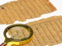 Dua lembar naskah kuno berbahasa Arab yang menguning dengan kaca pembesar di atasnya