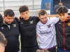 Ilustrasi sekelompok pemain sepak bola satu tim berangkulan membentuk lingkaran di pinggir lapangan bersama pelatihnya