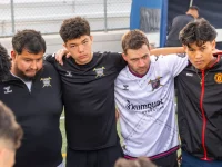Ilustrasi sekelompok pemain sepak bola satu tim berangkulan membentuk lingkaran di pinggir lapangan bersama pelatihnya