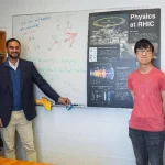 Para penulis studi berdiri di depan poster Physics at RHIC di Brookhaven National Laboratory.