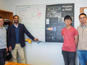 Para penulis studi berdiri di depan poster Physics at RHIC di Brookhaven National Laboratory.