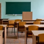 Deretan meja dan kursi kayu di ruang kelas dengan papan tulis hijau