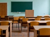 Deretan meja dan kursi kayu di ruang kelas dengan papan tulis hijau
