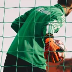 Penjaga gawang memegang bola di belakang jaring gawang saat latihan