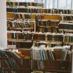 Deretan rak buku kayu di dalam ruang perpustakaan yang terang