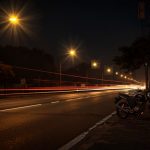 Ilustrasi jalan kota pada malam hari dengan lampu kekuningan dan garis cahaya kendaraan