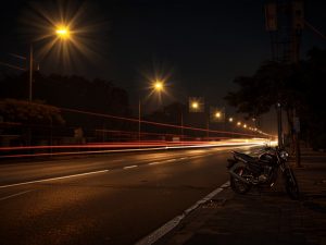 Ilustrasi jalan kota pada malam hari dengan lampu kekuningan dan garis cahaya kendaraan