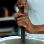 Ilustrasi juru masak mengaduk panci besar berisi nasi, bukan foto dapur MBG di Torosiaje
