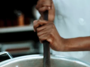 Ilustrasi juru masak mengaduk panci besar berisi nasi, bukan foto dapur MBG di Torosiaje
