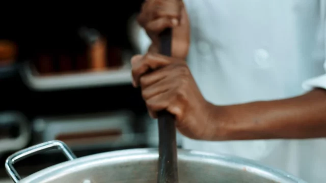 Ilustrasi juru masak mengaduk panci besar berisi nasi, bukan foto dapur MBG di Torosiaje