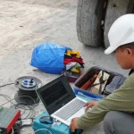 Peneliti bertopi keselamatan memantau data pada laptop saat persiapan demonstrasi guncangan gempa pada prototipe bangunan tahan gempa di Ponorogo.