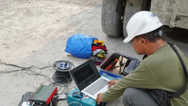 Peneliti bertopi keselamatan memantau data pada laptop saat persiapan demonstrasi guncangan gempa pada prototipe bangunan tahan gempa di Ponorogo.