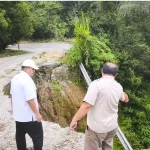 Dua orang meninjau badan jalan yang amblas dan longsor di kawasan perbukitan Sumatera Barat