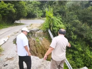 Dua orang meninjau badan jalan yang amblas dan longsor di kawasan perbukitan Sumatera Barat