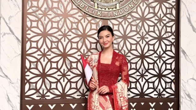 Raline Shah berkebaya merah sambil memegang bendera Merah Putih.