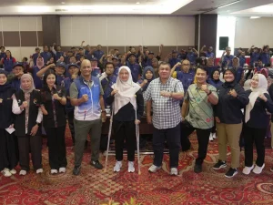 Peserta dan panitia kegiatan olahraga penyandang disabilitas berfoto bersama di dalam ruang pertemuan.