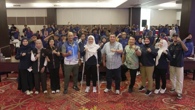 Peserta dan panitia kegiatan olahraga penyandang disabilitas berfoto bersama di dalam ruang pertemuan.