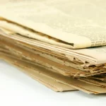 Tumpukan koran berusia seratus tahun dengan kertas menguning dan tepi yang sudah robek