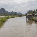 Sungai keruh di dataran rendah yang diapit tambak air payau dan perbukitan karst.