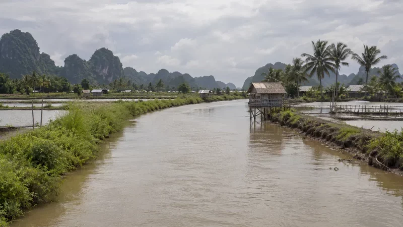 Sungai keruh di dataran rendah yang diapit tambak air payau dan perbukitan karst.
