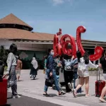Rombongan wisatawan menarik koper berjalan keluar dari area kedatangan berhias ornamen merah