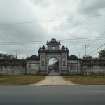 Ilustrasi sisa gerbang batu bekas istana Melayu di tepi jalan dikelilingi rumah baru