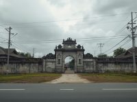 Ilustrasi sisa gerbang batu bekas istana Melayu di tepi jalan dikelilingi rumah baru