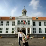 Gedung putih bekas balai kota Batavia dengan atap merah dan menara jam, dilihat dari Lapangan Fatahillah, Kota Tua Jakarta