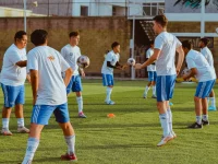 Ilustrasi sekelompok pemain sepak bola usia muda berlatih menggiring dan mengoper bola di lapangan rumput