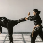 Ilustrasi dua atlet bela diri berseragam hitam bersabuk berlatih tendangan tinggi dan tangkisan di ruang latihan