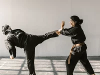 Ilustrasi dua atlet bela diri berseragam hitam bersabuk berlatih tendangan tinggi dan tangkisan di ruang latihan