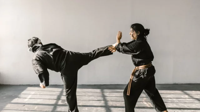 Ilustrasi dua atlet bela diri berseragam hitam bersabuk berlatih tendangan tinggi dan tangkisan di ruang latihan