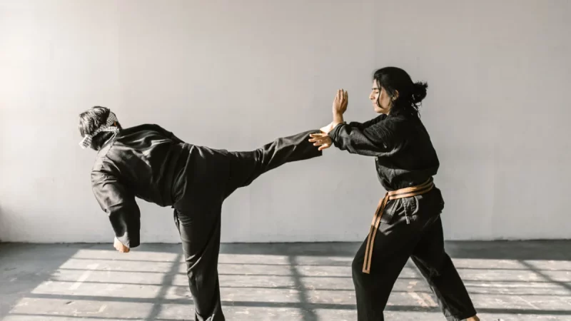 Ilustrasi dua atlet bela diri berseragam hitam bersabuk berlatih tendangan tinggi dan tangkisan di ruang latihan