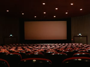 Deretan kursi merah menghadap layar bioskop yang menyala di ruang gelap