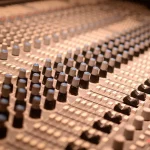 Deretan kenop dan fader pada meja mixer analog di ruang studio rekaman