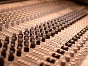Deretan kenop dan fader pada meja mixer analog di ruang studio rekaman