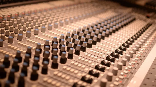 Deretan kenop dan fader pada meja mixer analog di ruang studio rekaman