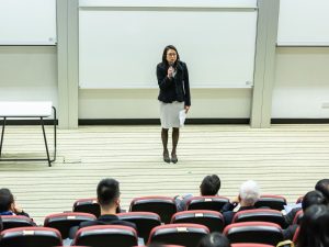 Ilustrasi seorang pembicara menyampaikan materi di hadapan peserta seminar pendidikan.