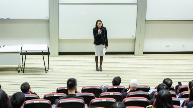 Ilustrasi seorang pembicara menyampaikan materi di hadapan peserta seminar pendidikan.