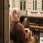 Seorang perempuan menikmati waktu sendiri di balkon sambil memandang kota.
